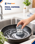 A hand uses a Shopkaart automatic dishwashing scrubber inside a black frying pan filled with soapy water in a kitchen sink. The Shopkaart brand logo and the text 'PRESS.
