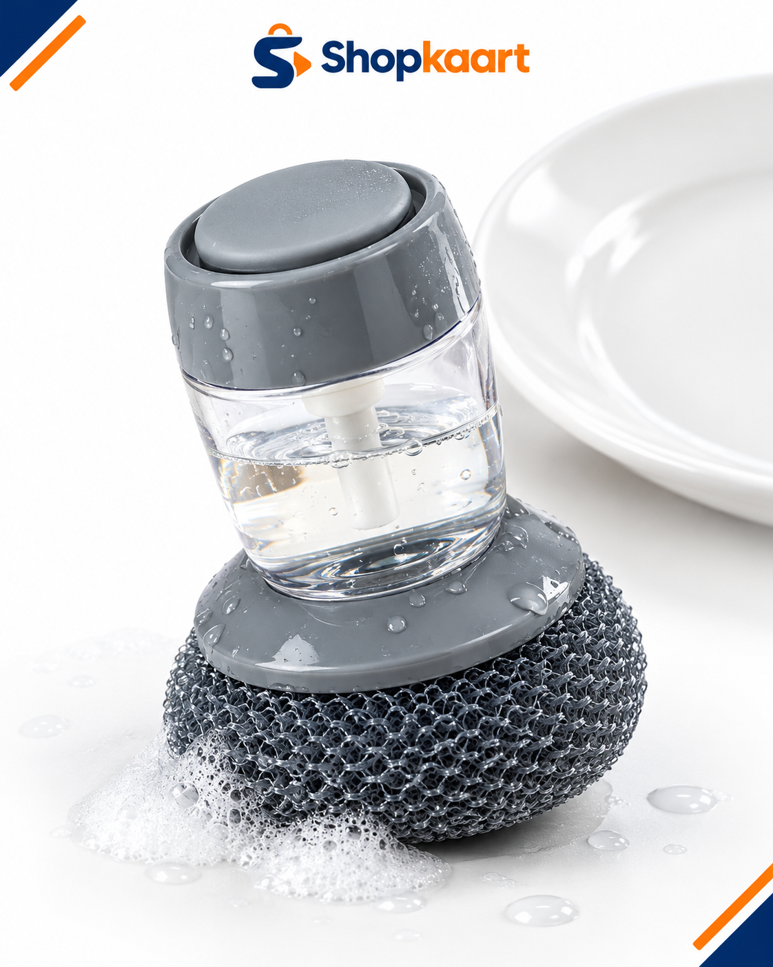 A small countertop cleaning brush with a gray textured bristle base, a clear cylindrical container filled with liquid, and a gray flip-top lid. Foaming soap is visible at the base, and a white plate appears in the background.